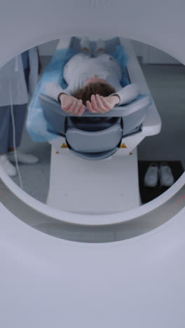 Vertical-shot-of-female-patient-on-CT,-PET,-or-MRI-bed-moving-inside-machine.-Advanced-tools-scan-body-and-brain-for-detailed-examination-in-a-healthcare-facility.-High-tech-modern-medical-technology.